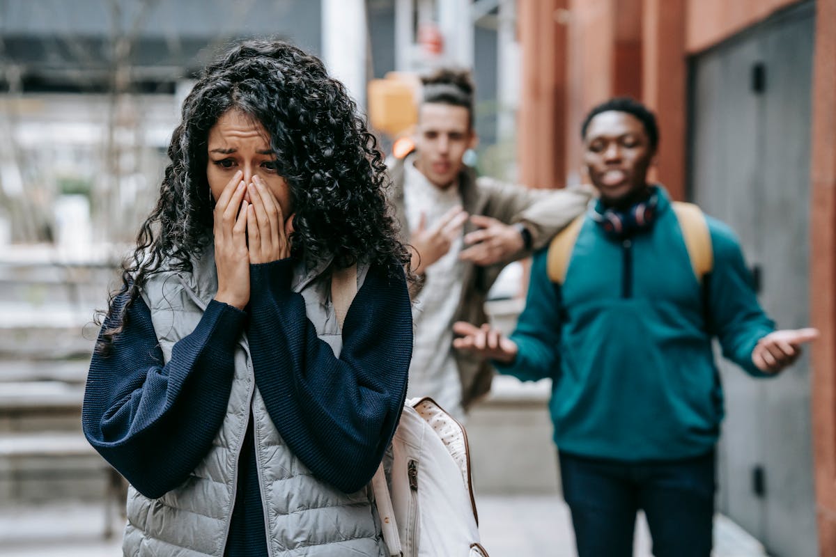 Sad ethnic woman crying after being bullied by multiracial male students