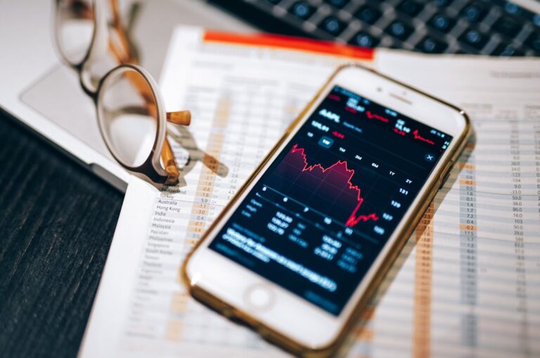 Smartphone displaying stock market chart on a financial spreadsheet with eyeglasses.
