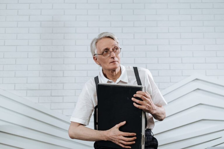 Elderly man in glasses and suspenders holding a briefcase in a modern office setting.