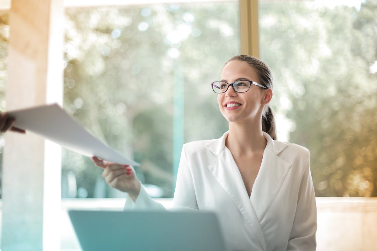 Smiling businesswoman in a modern office handing over documents, symbolizing professionalism and teamwork.