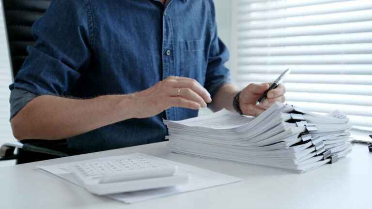 Person working at an office desk. Analyzing financial data. Calculating figures with a calculator. And signing multiple paper documents. Representing the concepts of accounting. Auditing